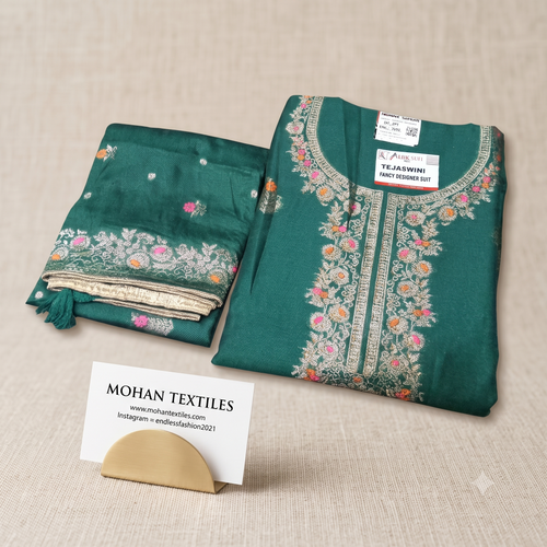 Folded Bottle green unstitched silk suit material with intricate zari neck embroidery and matching floral border dupatta on textured beige linen background