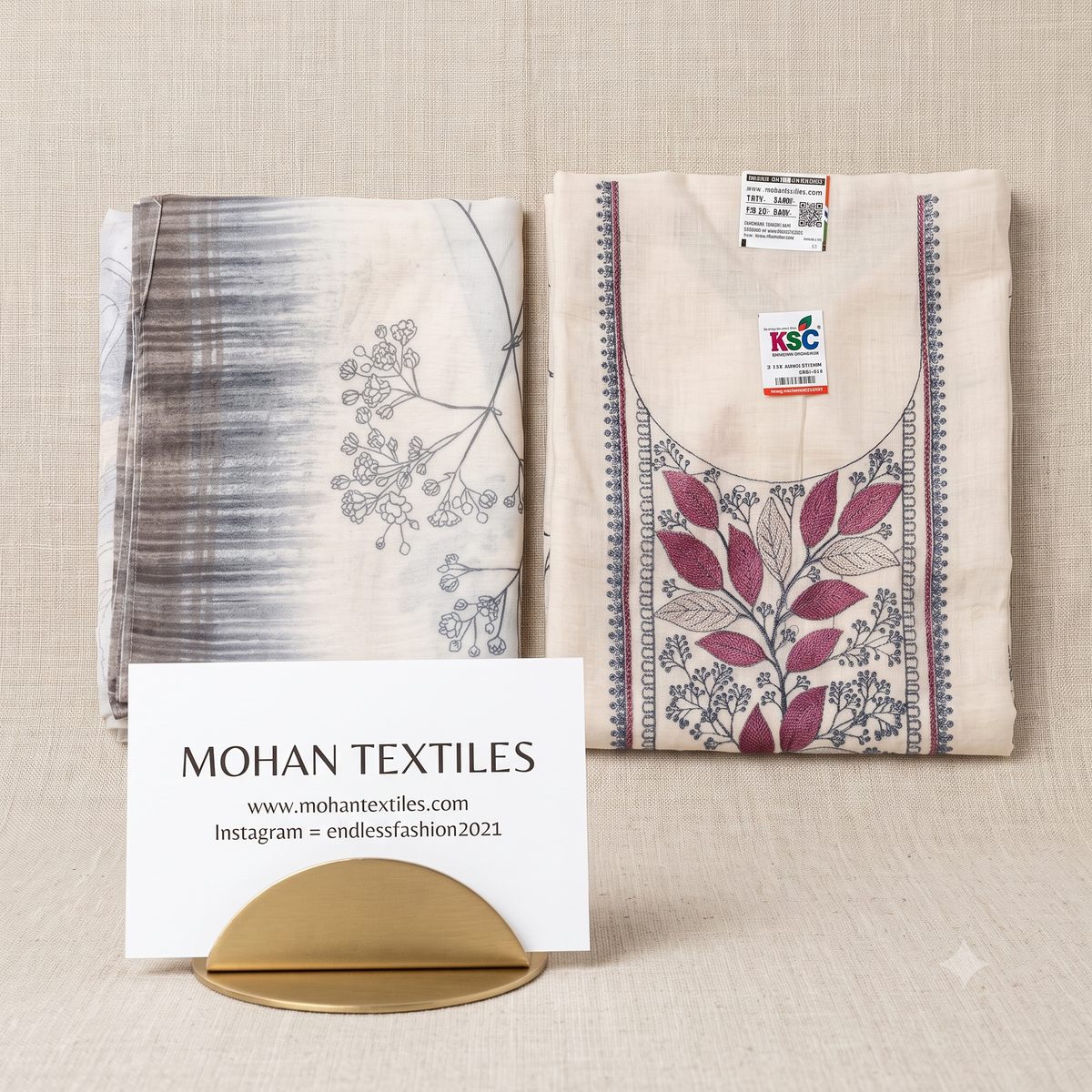 Flat lay product photography of an off-white unstitched linen suit set, showing the detailed purple and blue thread embroidery on the kurta piece next to a patterned dupatta, by Mohan Textiles.
