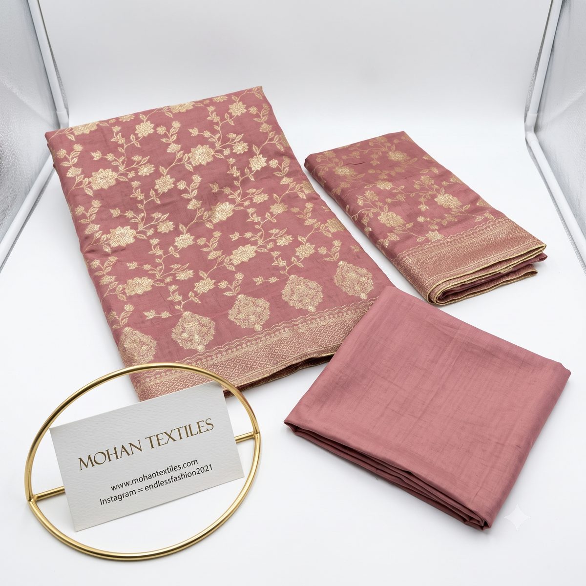 Flat lay of Dusty Rose unstitched Banarasi style party wear dress material, featuring intricate gold zari floral weaving and a matching dupatta, available at Mohan Textiles.