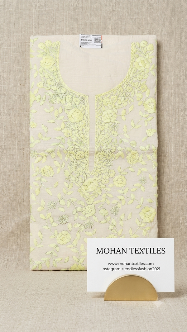 A Lemon-colored cotton fabric kurta laid flat on a beige textured background, featuring light green floral embroidery around the neckline and down the front. A white card displaying 'MOHAN TEXTILES' is placed in front of the garment.