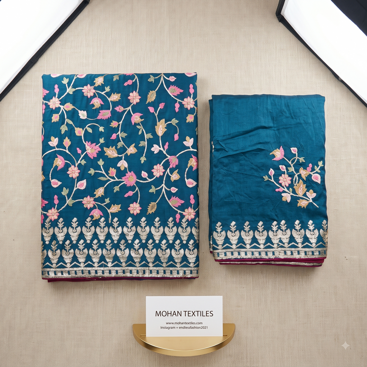Unstitched Punjabi Dress Material of teal blue floral silk fabric displayed side by side on a beige textured surface, with a small card reading MOHAN TEXTILES below them.