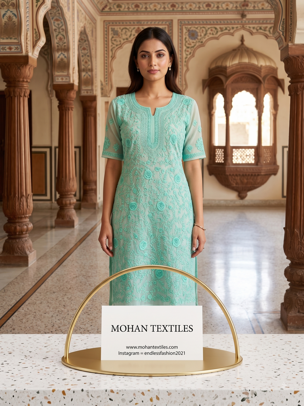A woman stands indoors wearing a light aqua phulkari embroidered kurta with short sleeves and a split neckline. She is posed in front of ornate architectural pillars and a carved wooden alcove.