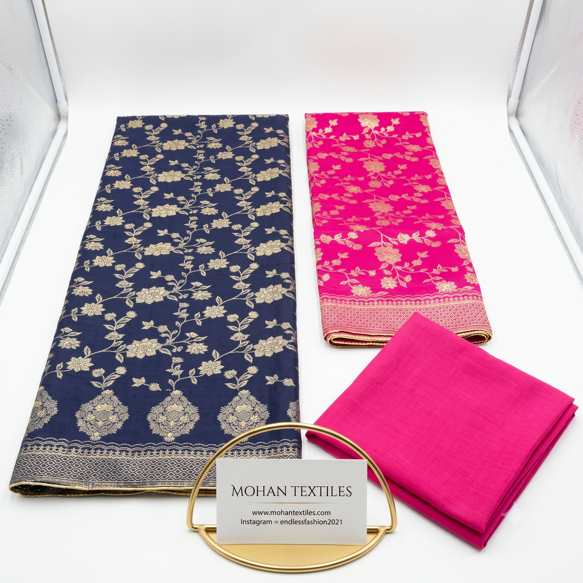 Flat lay of Navy Blue & Pink unstitched Banarasi style party wear dress material, featuring intricate gold zari floral weaving and a matching dupatta, available at Mohan Textiles.