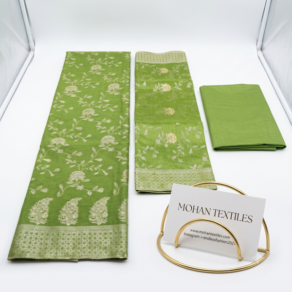Flat lay of Pistachio Green unstitched Banarasi style party wear dress material, featuring intricate gold zari floral weaving and a matching dupatta, available at Mohan Textiles.