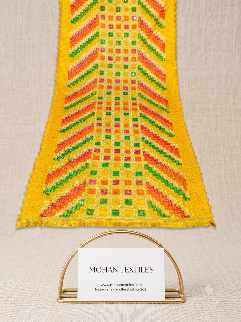 A close-up of a yellow Phulkari Dupatta with colorful geometric patterns in green, orange, pink, and red, displayed on a neutral textured background with a MOHAN TEXTILES brand card below.