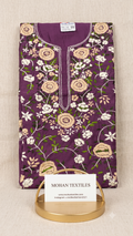 A folded purple phulkari embroidered kurta or tunic with floral and vine motifs, displayed on a gold stand with a white card labeled MOHAN TEXTILES. The fabric is laid flat on a light beige textured background.