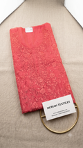 A folded coral pink phulkari embroidered kurta fabric, displayed on a beige textured fabric surface with a white brand card reading MOHAN TEXTILES and a gold ring stand.