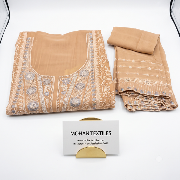 A folded beige traditional embroidered fabric set on a white background, including a blouse piece with ornate embroidery and a matching dupatta. A small card reading MOHAN TEXTILES is placed in front.