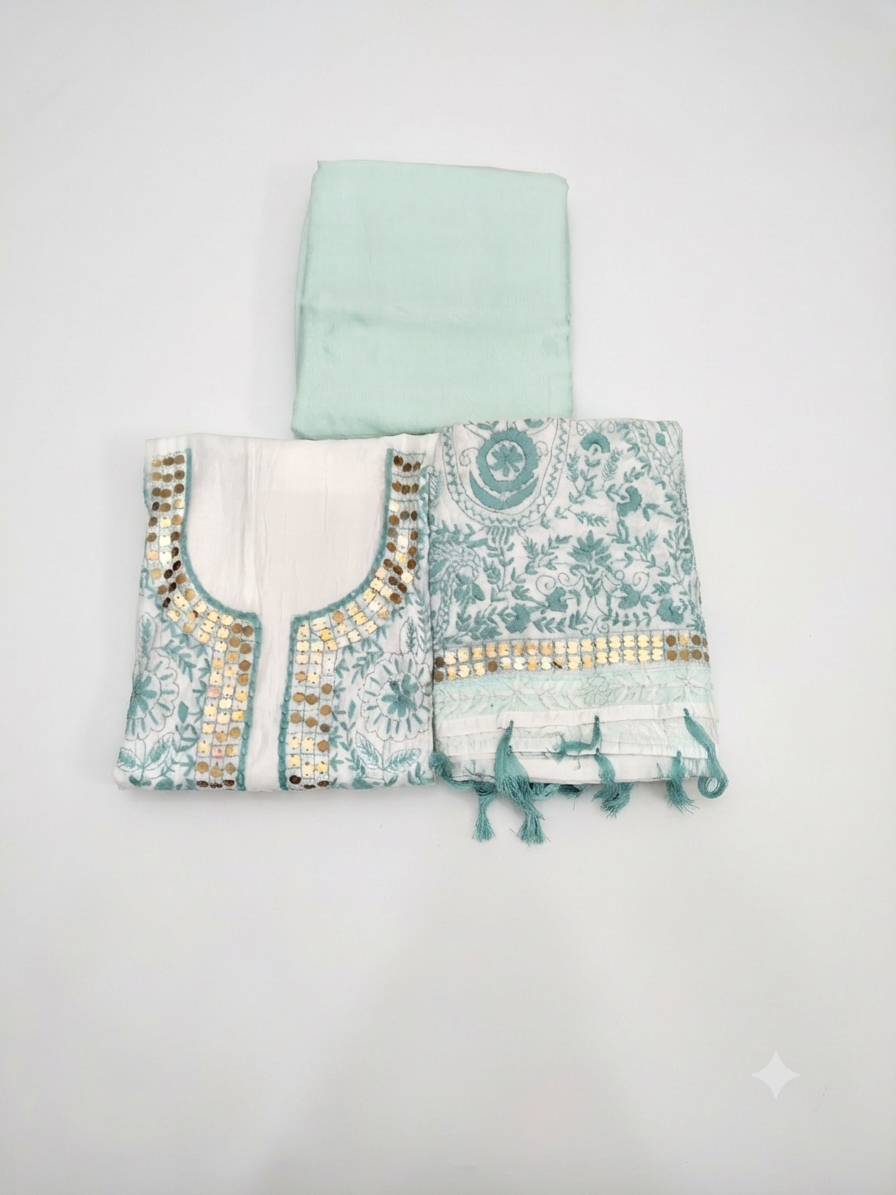 A folded traditional outfit set on a plain light background, featuring a mint green fabric piece at the top and a patterned kurta-style top with matching fabric below. The garment has a white base with teal-blue floral and paisley motifs, teal border detailing, and small gold mirror-like embellishments.